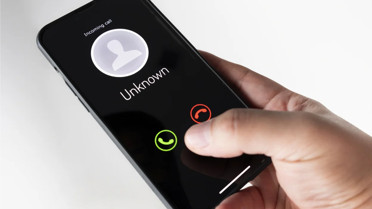 Smartphone screen showing a scam or unknown caller warning with a laptop in the background